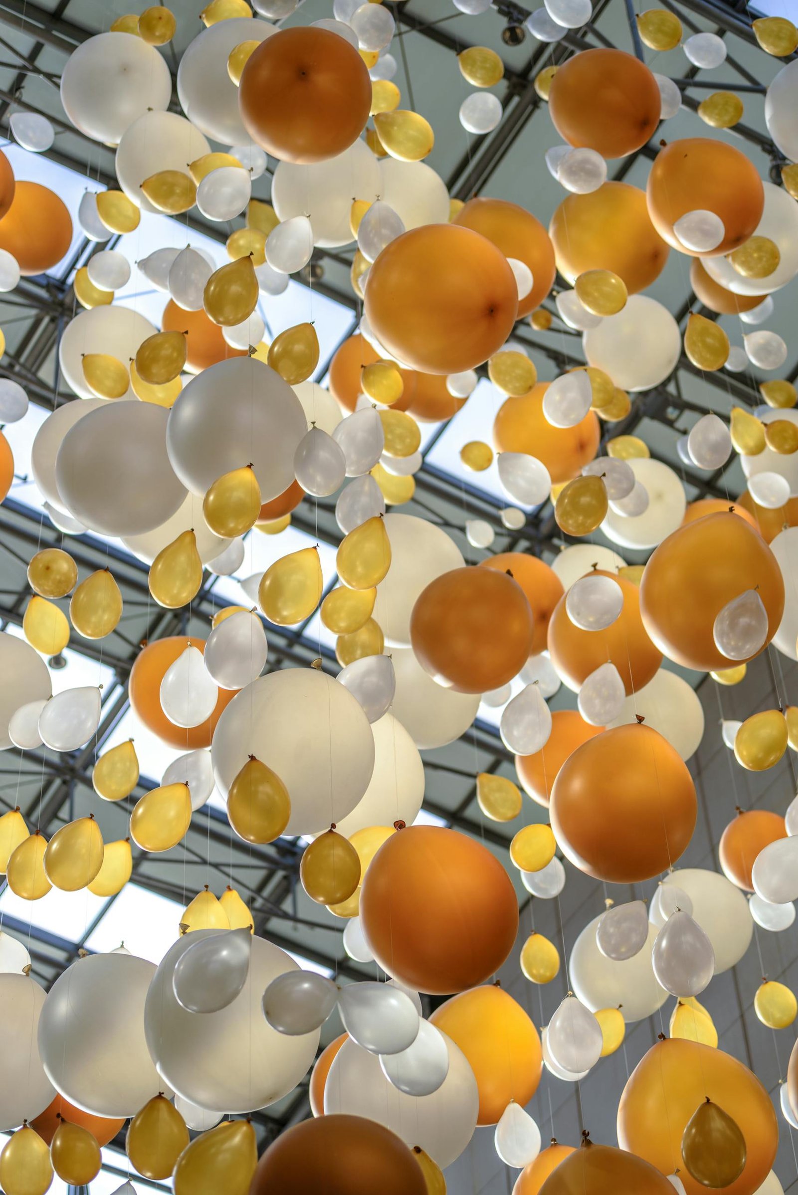 Vibrant arrangement of orange, white, and yellow balloons hanging in an indoor celebration space.